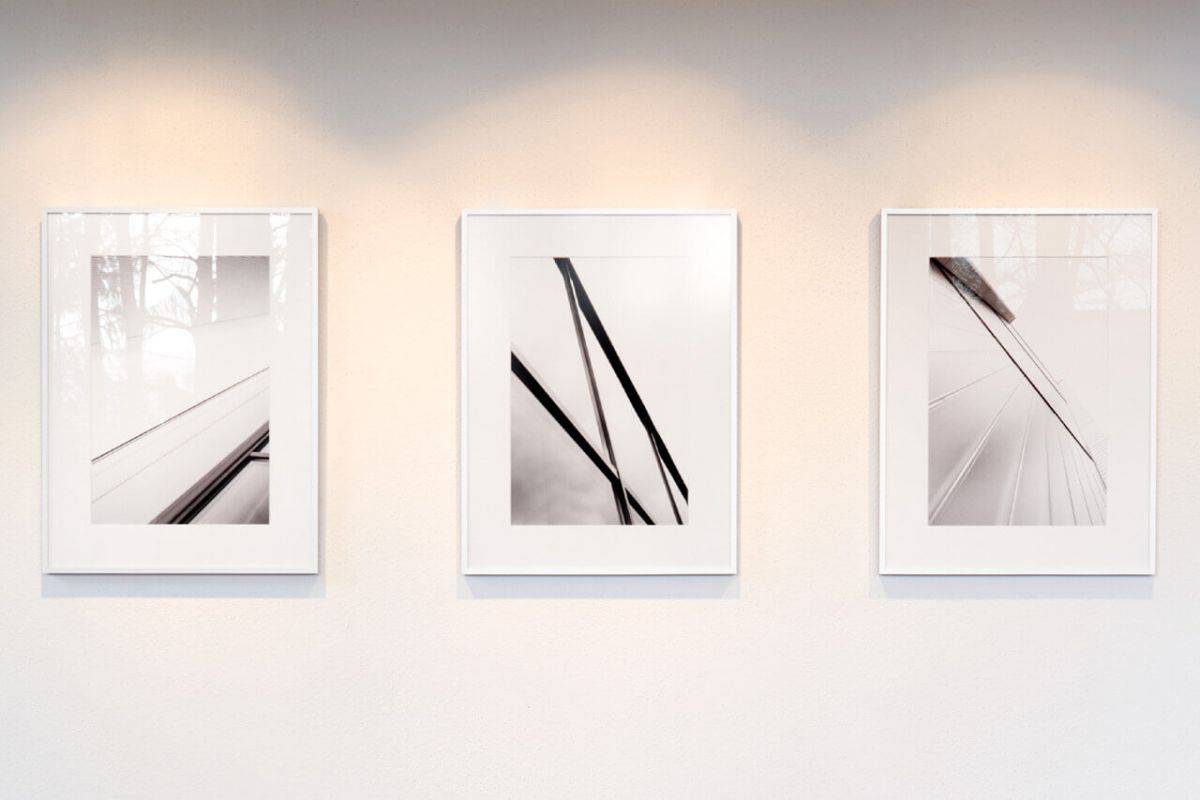 Im Bild zu sehen sind drei Rahmen gegenüber eines Fensters: v.l.n.r. Normalglas glänzend, Weißglas einseitig matt, Museumsglas entspiegelt.