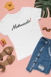 Weißes T-Shirt mit Aufdruck "Mettmoiselle!" umgeben von weiteren Kleidungsstücken