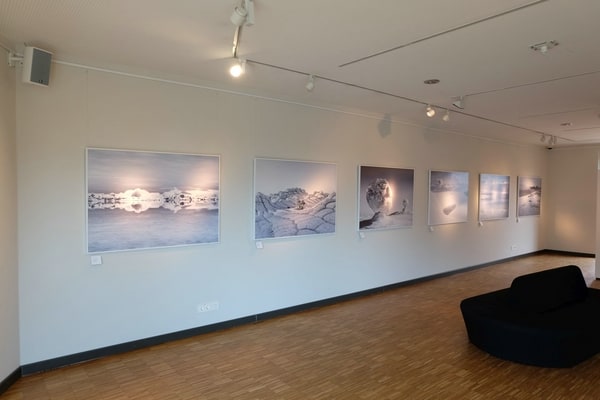 Ansicht der Ausstellung Into the Light von Tom Jakobi: 6 Bilder an heller Wand, davor dunkles Sofa auf Holzboden