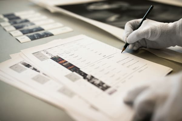 Behandschuhte Hand hält Bleistift und hakt Liste der Exponate ab