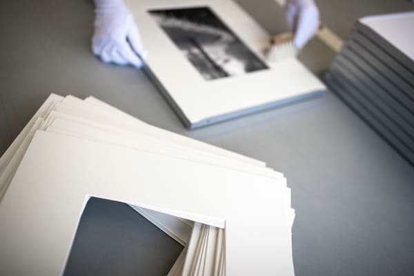 Behandschuhte Hände rahmen ein Bild mit Passepartout. Im Vordergrund ein Stapel heller Passepartouts, die auf ihren Einsatz warten