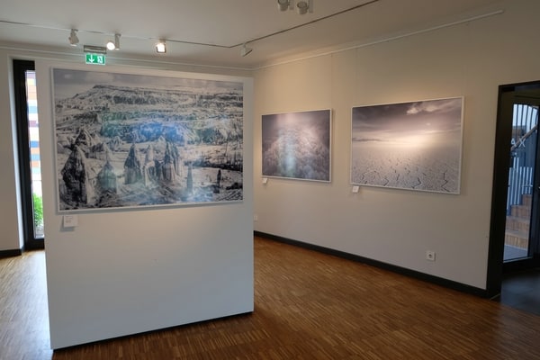 Ansicht der Ausstellung Into the Light von Tom Jakobi: Bild an Raumteiler, im rechten Winkel dazu 2 Bilder an heller Wand, alle im gleichen Format