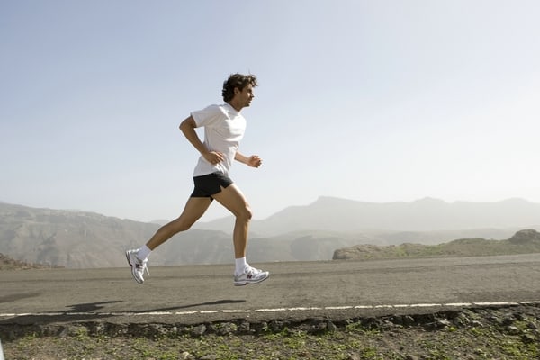 Läufer in Sportkleidung auf Asphaltstraße vor Landschaft