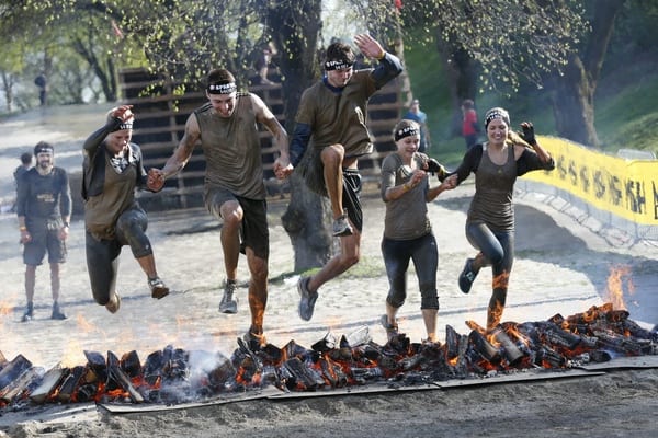 5 Sportler springen nebeneinander über eine niedrige Feuerbarriere