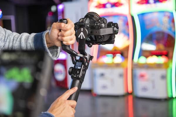 Mann hält Manfrotto Gimbal mit beiden Händen und filmt. Im Hintergrund verschwommene, farbenfrohe Kulisse