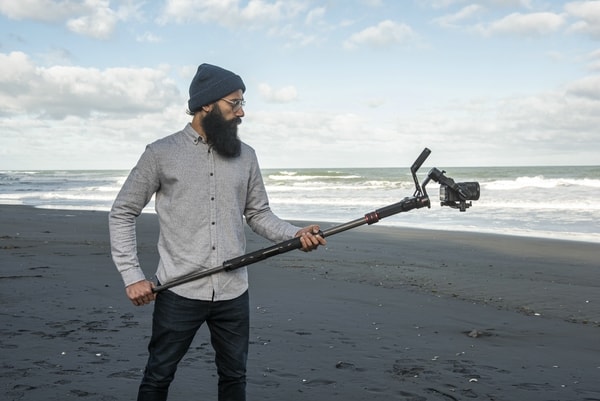 Szene an leerem Strand: Mann filmt mit Manfrotto Gimboom in beiden Händen