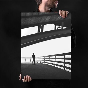 Ein Mann hält ein hochformatiges, kontrastreiches Schwarzweiß-Wandbild einer modernen Brückenarchitektur vor sich. Ein Mann hält ein hochformatiges, kontrastreiches Schwarzweiß-Wandbild einer modernen Brückenarchitektur vor sich.