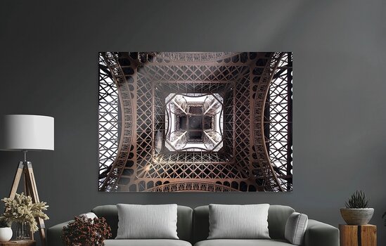 Ein großformatiges, glänzendes Acrylglas-Wandbild mit der Innenansicht des Eiffelturms, aufgehängt an einer dunkelgrauen Wand über einer Couch. Ein großformatiges, glänzendes Acrylglas-Wandbild mit der Innenansicht des Eiffelturms, aufgehängt an einer dunkelgrauen Wand über einer Couch.