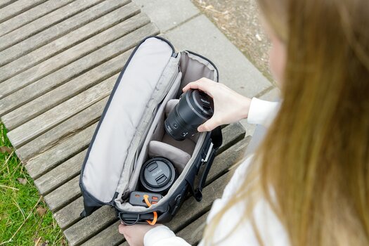 Eine Person verstaut ein Objektiv im gepolsterten Innenraum der geöffneten Rollei Fotoliner Ocean Rolltop Bag L. Eine Person verstaut ein Objektiv im gepolsterten Innenraum der geöffneten Rollei Fotoliner Ocean Rolltop Bag L.