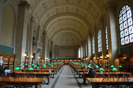 Der symmetrische Lesesaal Bates Hall der Boston Public Library mit grünen Tischlampen, hohen Rundbogenfenstern und historischen Holztischen. Der symmetrische Lesesaal Bates Hall der Boston Public Library mit grünen Tischlampen, hohen Rundbogenfenstern und historischen Holztischen.