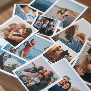 Mehrere ausgedruckte Familien- und Urlaubsfotos liegen verteilt auf einem Holztisch.