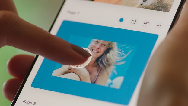 Eine Person gestaltet auf einem Smartphone eine Fotobuchseite und verschiebt ein Bild mit dem Finger.