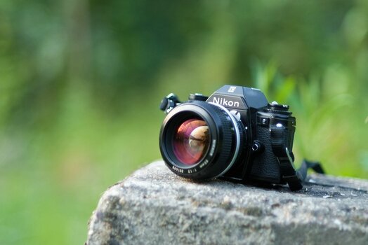 Nikon-Spiegelreflexkamera mit lichtstarkem Objektiv auf einem Stein im Grünen – Symbolbild zum Tag der Kamera.