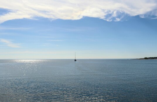 Ein einzelnes Segelboot auf dem offenen Meer vermittelt Minimalismus, Ruhe und die Sehnsucht nach der Ferne
