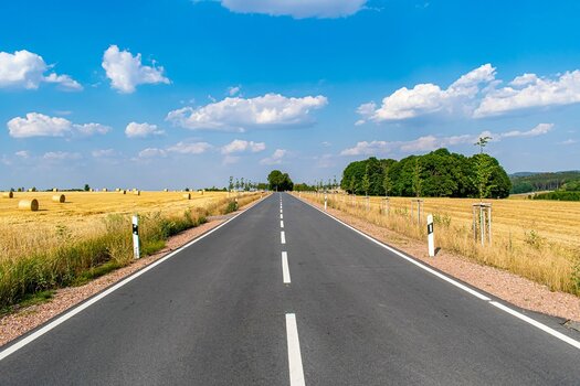 Gerade Landstraße führt durch eine sommerliche Landschaft und symbolisiert Aufbruch und Abenteuer.
