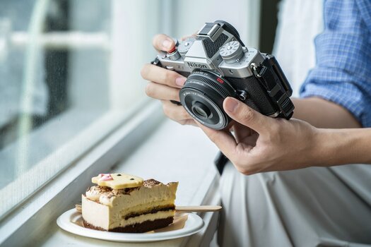 Nikon Zf mit angesetztem Viltrox AF 26 mm F2.8 EVO neben einem Stück Kuchen auf einer Fensterbank. Nikon Zf mit angesetztem Viltrox AF 26 mm F2.8 EVO neben einem Stück Kuchen auf einer Fensterbank.