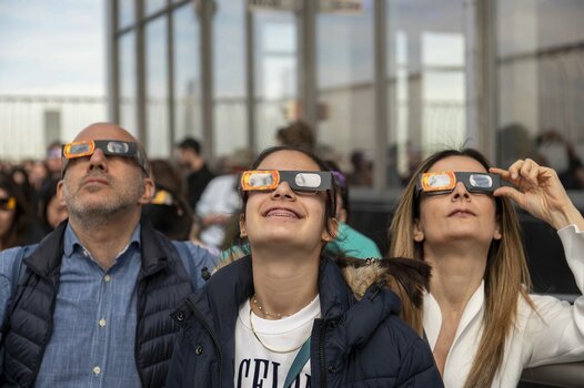 Drei Menschen beobachten eine Sonnenfinsternis mit speziellen Sonnenfinsternisbrillen. Drei Menschen beobachten eine Sonnenfinsternis mit speziellen Sonnenfinsternisbrillen.