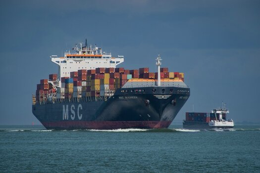 Großes Containerschiff neben einem deutlich kleineren Schiff auf dem Wasser Großes Containerschiff neben einem deutlich kleineren Schiff auf dem Wasser