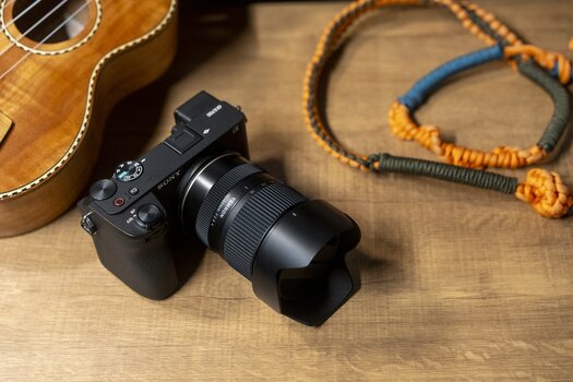 Sony-Kamera mit TAMRON 16–50mm F2.8 A auf einem Holztisch neben einer Ukulele. Sony-Kamera mit TAMRON 16–50mm F2.8 A auf einem Holztisch neben einer Ukulele.