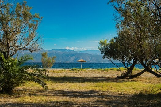 Mediterrane Küstenlandschaft mit Bäumen, Strand und Sonnenschirm vor blauem Meer und Bergen, optimiert mit Luminar Enhance AI. Mediterrane Küstenlandschaft mit Bäumen, Strand und Sonnenschirm vor blauem Meer und Bergen, optimiert mit Luminar Enhance AI.