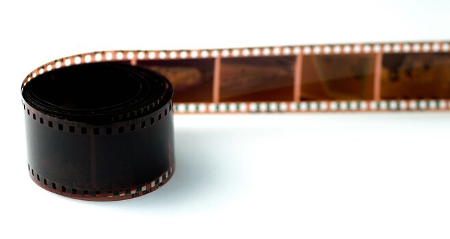 Aufgerollter analoger Farbnegativfilm mit einem ausgerollten Filmstreifen auf hellem Hintergrund.