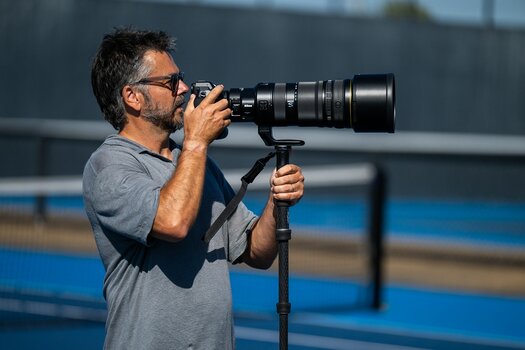 Fotograf hält eine Nikon-Z-Kamera mit NIKKOR Z 120-300mm f/2.8 TC VR S auf einem Einbeinstativ.