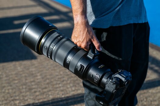 Person trägt eine Nikon-Z-Kamera mit angesetztem NIKKOR Z 120-300mm f/2.8 TC VR S am Stativfuß.