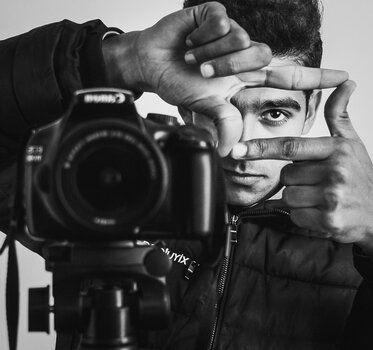 Mann posiert hinter DSLR auf Stativ