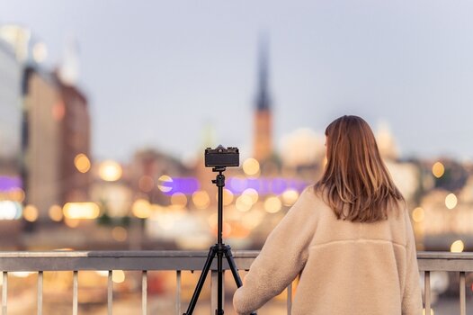 Szenebild: Fotografin mit Kamera auf Velbon-Stativ vor unscharfer Stadtkulisse