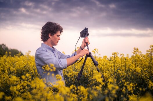 Szenebild: Fotograf in Feld mit gelben Blüten beim Aufbau eines Velbon-Stativs