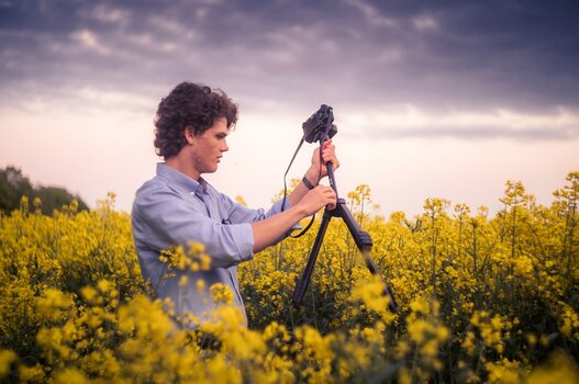 Szenebild: Fotograf in Feld mit gelben Blüten beim Aufbau eines Velbon-Stativs Szenebild: Fotograf in Feld mit gelben Blüten beim Aufbau eines Velbon-Stativs
