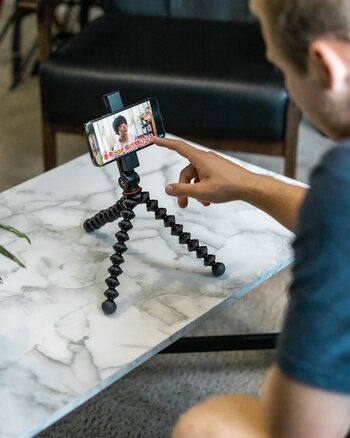 Mann bedient Smaprtphone mit GripTight GorillaPod für MagSafe auf niedrigem Tisch Mann bedient Smaprtphone mit GripTight GorillaPod für MagSafe auf niedrigem Tisch