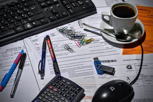 Papierkram, Taschenrechner, Tasse Kaffee vor dem PC - Symbolbild für Verwaltungsarbeiten als Selbstständiger