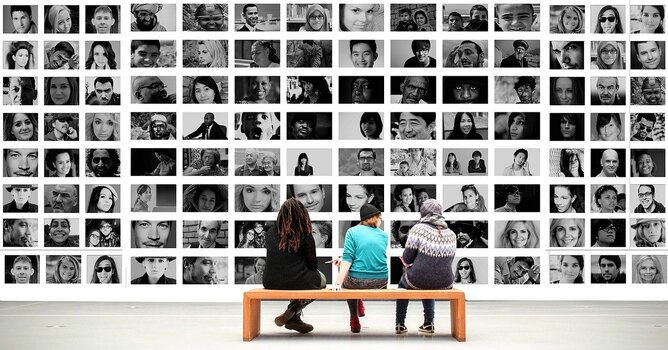 Drei Menschen, auf Holzbank sitzend, betrachten Wand mit Fotocollage von Portraits Drei Menschen, auf Holzbank sitzend, betrachten Wand mit Fotocollage von Portraits
