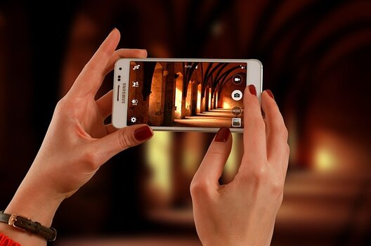 Frauenhände halten Smartphone zum Fotografieren eines Kreuzgangs