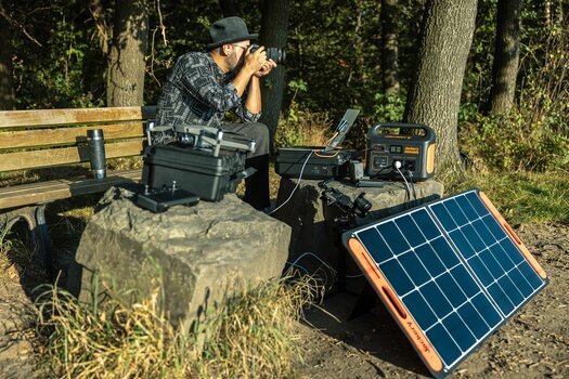 Mann sitzt auf einer Bank und fotografiert. Um ihn  herum Fotoequipment sowie ein Solargenerator von Jackery und ein Solarpanel 
