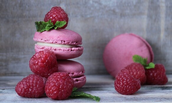 Rosa Macarons mit Himbeeren garniert vor hellgrauem Hintergrund