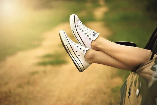 Frau steckt Füße in Sneakers aus Autofenster