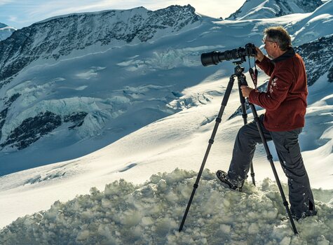 Mann fotografiert Schneelandschaft mit Kamera auf Stativ Rock Solid Alpha Mark III Mann fotografiert Schneelandschaft mit Kamera auf Stativ Rock Solid Alpha Mark III