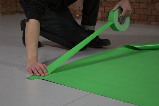 Detailaufnahme beim Studioaufbau: Mann klebt Untergrund mit  Gaffer Tape 50mm x 50m Chromakey Grün auf den Boden. 