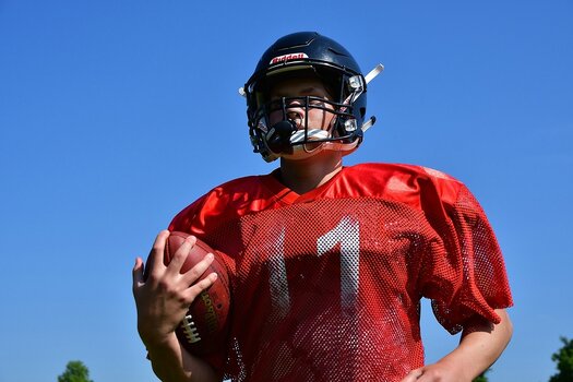 Starke Farb- und Lichtkontraste bei hartem Sonnenlicht: American Footballspieler in rotem Trikot, dunklem Helm von unten gegen strahlend blauen Himmel fotografiert