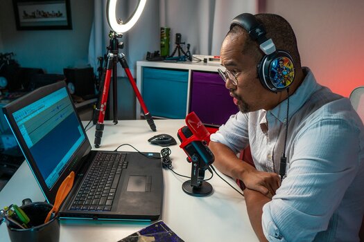 Mann sitzt an Schreibtisch vor Laptop und Joby Wavo Pod Mann sitzt an Schreibtisch vor Laptop und Joby Wavo Pod