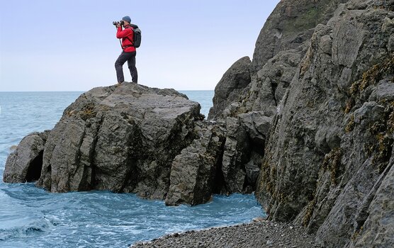 Mann auf ins Meer ragendem Felsvorsprung mit Kamera und Steadify bei der Outdoorfotografie