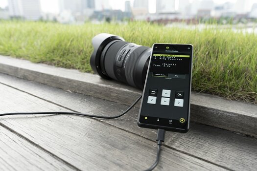 Smartphone mit Tamron-App ist an Objektiv angeschlossen
