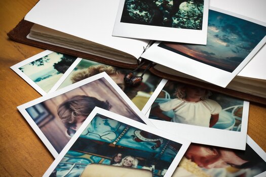 Polaroidbilder auf einem Tisch verstreut, im Hintergrund ein Fotoalbum