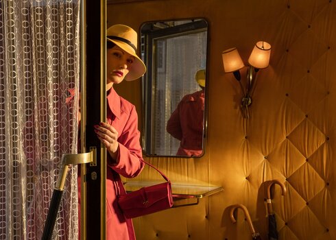 Frau In Mantel mit Handtasche und Hut schaut an der sich öffnenden Tür in den Raum. Ca. 1950er-Jahre-Szenario