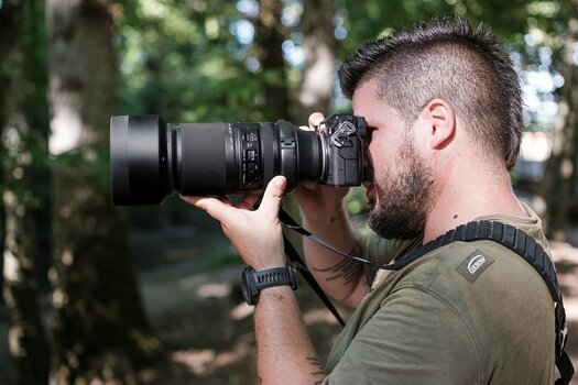 Mann fotografiert freihand mit dem TAMRON 150-500mm F/5-6.7 Di III VC VXD für X-Mount an einer Fujifilm-Kamera Mann fotografiert freihand mit dem TAMRON 150-500mm F/5-6.7 Di III VC VXD für X-Mount an einer Fujifilm-Kamera