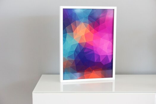 pink-blau-rotes grafisches Bild in einem weißen Bilderrahmen, der auf einer weißen Kommode präsentiert wird.