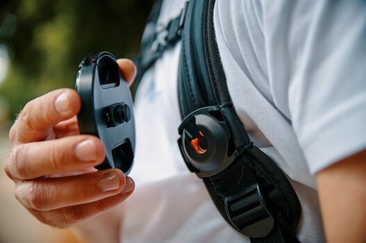 Detailbild: Mann sichert Objektivdeckel am SNAPSNAP lens cap clip an seinem Rucksacktrageriemen