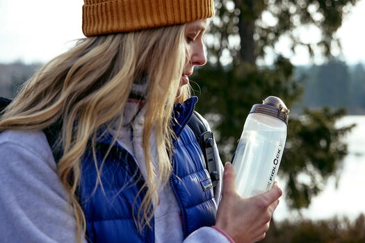 Frau befestigt Trinkflasche an der Halterung TWIST tex base multi an ihrem Rucksackgurt